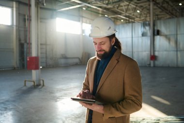 Genç, kendine güvenen müteahhit ya da depo sahibi, online bilgiler ya da teknik çizimler içeren belgeler aracılığıyla tablete kayıyor.