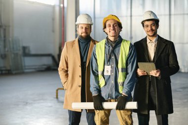 Kültürler arası mutlu bir grup genç adam kameraya bakıp geniş bir deponun duvarına ve köşesine bakıyorlar.