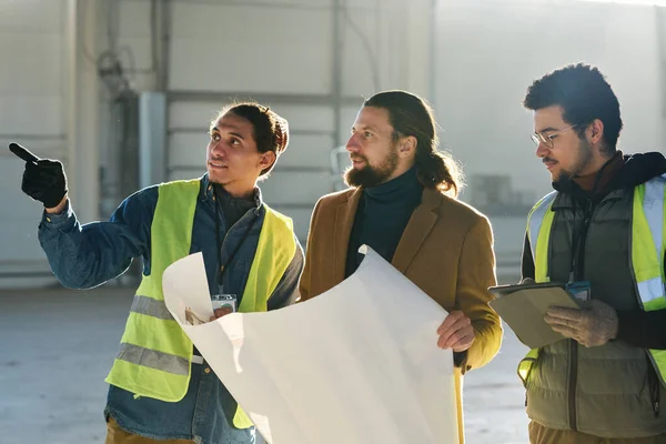 Young Engineer Contractor Blueprint Listening Warehouse Worker Pointing Something Explanation — Stock Photo, Image