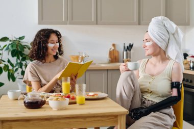Mutfak masasının yanında oturan, abur cubur ve içeceklerle servis edilen, kahvaltıya kadar sohbet edip kitap okuyan, göz bandı takan iki tatlı kız arkadaş.