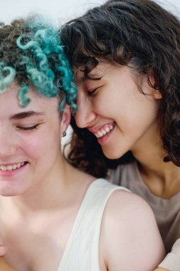 İki kültürler arası neşeli kızın kamera önünde gülüşünü yakından çekerken esmer genç bir kadın sevgilisinin arkasında duruyor.