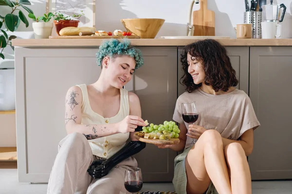 Myoelektrik eli olan mutlu genç bir kadın elinde kırmızı şarapla güzel kız arkadaşının tuttuğu tahtadan yeşil üzümler alıyor.