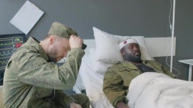 Üzgün Kafkas askeri, askeri hastanede ciddi beyin hasarı olan Afrikalı Amerikalı arkadaşını ziyaret ediyor.