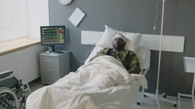 Kafasında kurşun yarası olan baygın Afro-Amerikan askeri modern askeri hastanede yatakta yatıyor.