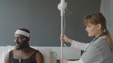 Kafkasyalı genç hemşire, askeri hastanedeki Afrikalı Amerikalı hastaya damar içi tedaviye başlamak için serum ve tüple direk getiriyor.