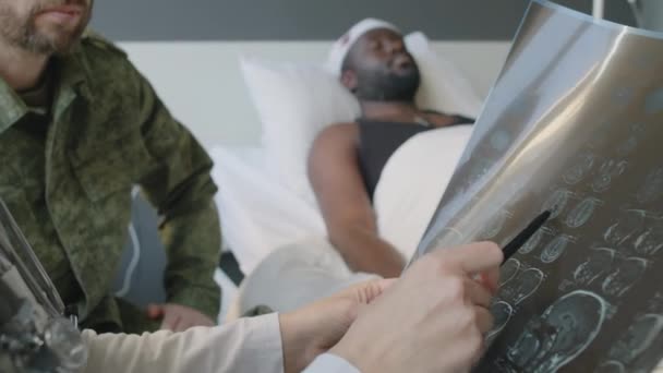 意識不明の患者を抱える 認識できない軍病院の開業医の選択的な焦点ショット 彼の友人との会話を持つ脳X線画像 — ストック動画