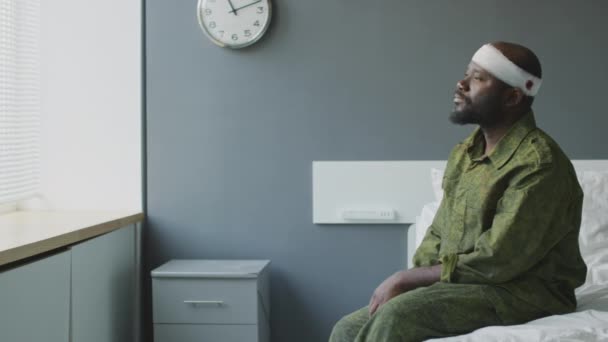 一名头戴迷彩服 头戴枪伤的黑人军人坐在医院病房的病床上思考自己的未来 — 图库视频影像