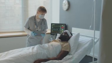 Kafkasyalı genç kadın doktor hastane odasında başından yaralanan siyahi bir adamın sağlık durumunu kontrol ediyor.