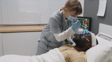 Doktor maske takıp göz bebeği tepkisini kontrol ediyor. Sonra da Afrika kökenli Amerikalı hastaya kalp kapakçığı maskesi takıp yapay havalandırma yapıyor.