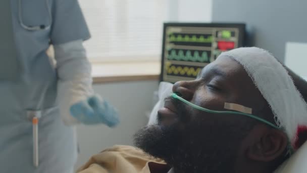 医者と話す病院のベッドに横たわる頭部負傷のひげ付きアフリカ系アメリカ人男性の選択的な焦点のクローズアップ — ストック動画