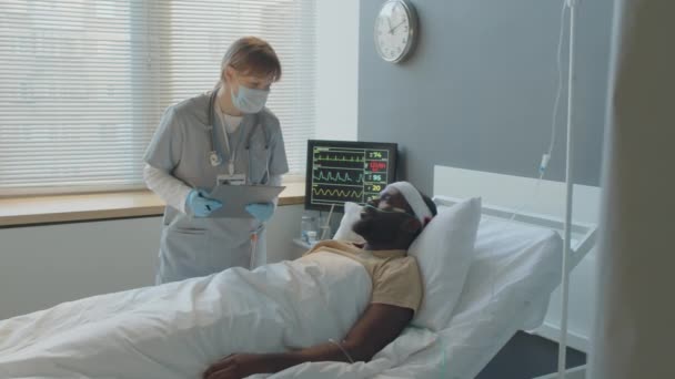 若い白人女性医師が病院の部屋で頭部負傷した黒人の健康状態をチェック — ストック動画