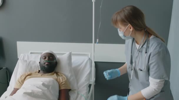 マスクを着用している白人看護師は 頭部損傷を伴う無意識の背中の患者のための薬液をIvラインに追加します — ストック動画