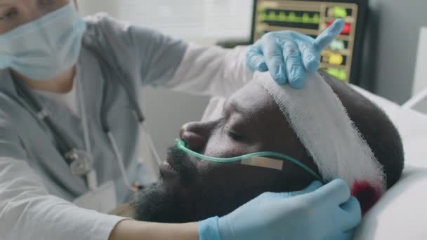頭部損傷の無意識のアフリカ系アメリカ人男性のための包帯および鼻腔を点検し 固定する医師の選択的な焦点の閉鎖 — ストック動画