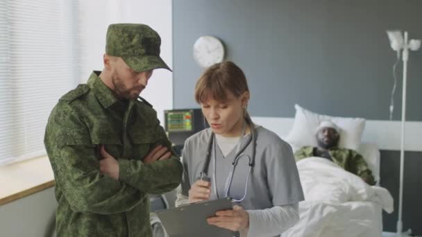 Żołnierz Kaukaski Omawia Sposoby Leczenia Swojej Nieprzytomnej Przyjaciółki Lekarzem Szpitalu — Wideo stockowe