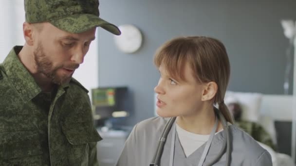 軍の病院で医師と彼の負傷した友人の健康状態と治療を議論する心配した軍人の選択的な焦点 — ストック動画