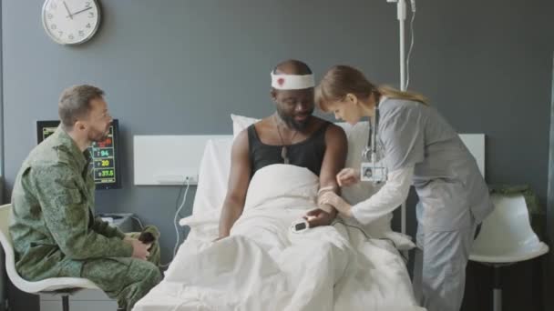 Ivライン針を患者の静脈に挿入する看護師は 親友とチャットしながら 軍病院のコンセプトで治療 — ストック動画