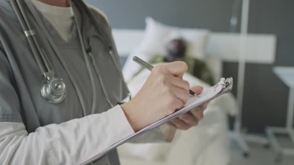 白种人女医生居中特写站在军医院病房填写病人医疗卡 — 图库视频影像