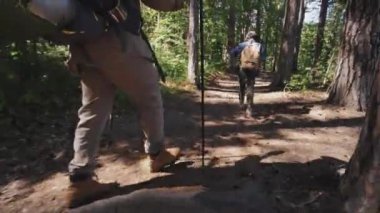 Aktif siyah adam ve çocuğun, yaz günü dağ ormanlarında yürüyüş direkleri ile sırt çantaları takıp yürüyüş yaparken çekilmiş görüntüleri.