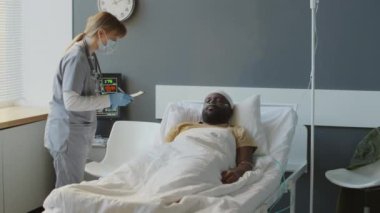 Genç, Afro-Amerikan, kafa yaralanması geçiren bir hastanın sağlık durumunu kontrol eden kadın doktor.
