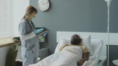 Dijital tablet tutan cerrah askeri hastanede Afrikalı Amerikalı bir hastanın sağlık durumunu kontrol ediyor.