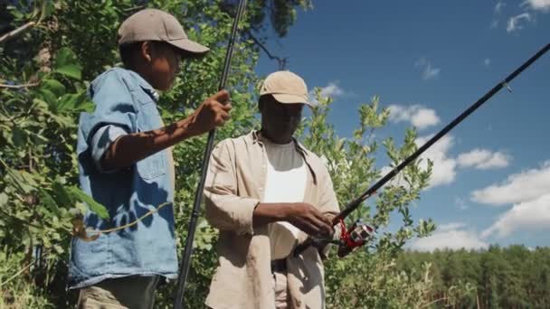 アフリカ系アメリカ人の祖父が孫に釣り棒を投げる方法を教える低角度ビュー中型ショット — ストック動画