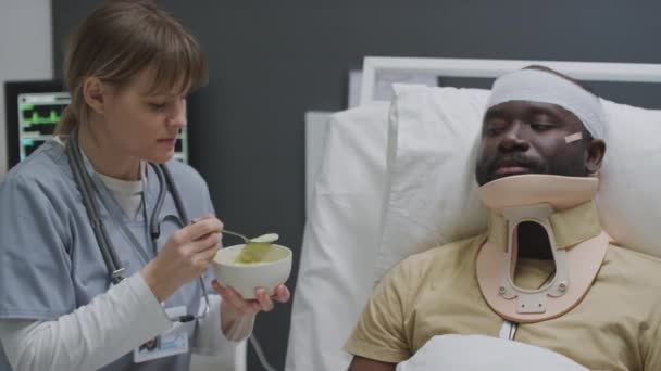 Profesional Enfermera Cuchara Alimentación Lesionado Afroamericano Hombre Con Vendaje Cabeza — Vídeos de Stock