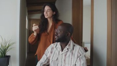 Orta boylu, siyah saçlı, beyaz bir kadın penceresinden ona gülümseyen Afro-Amerikan gözlüklü adama bakıyor.