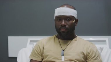 Kafasından yaralanmış Afro-Amerikan askerinin orta boy portresi askeri hastane odasında kameraya bakıyor.