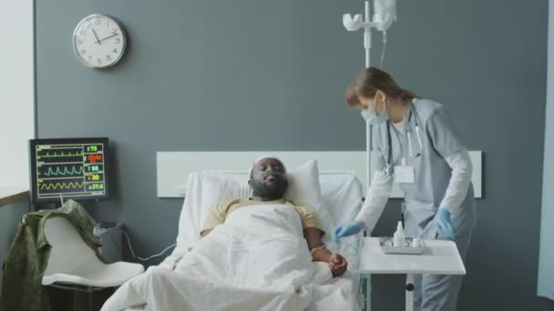 軍病院のアフリカ系アメリカ人患者のためのIvバッグに薬を添加する看護師の中長ショット — ストック動画
