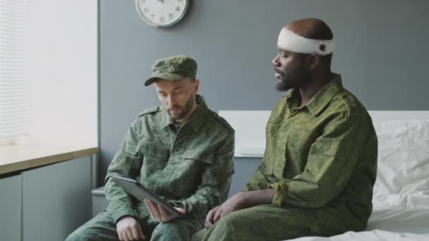 軍病院で負傷した黒人の同僚を訪ねたコーカサス中尉がデジタルタブレットでニュースを見せた — ストック動画