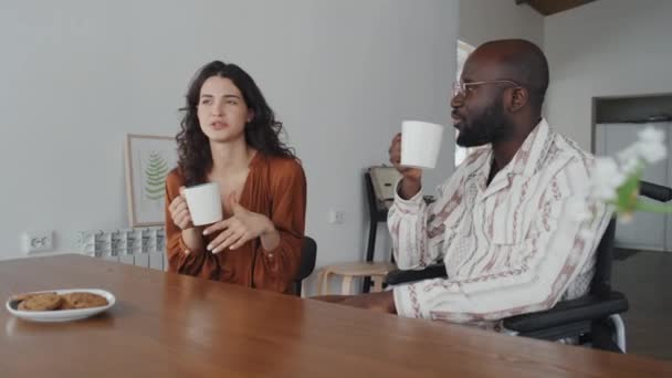 アフリカ系アメリカ人は 友好的な会話をしながら 自宅で紅茶やコーヒーを一緒に持っている男と白髪の女性を標的にしました — ストック動画