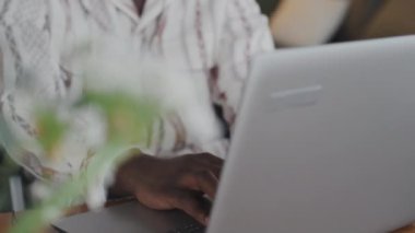 Kulaklıkla müzik dinleyen, dizüstü bilgisayarında daktilo yazan siyah gözlüklü adamın gevşek yakın çekimi.