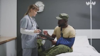 Kol askısı takan Afrikalı Amerikalı asker hastaneden taburcu oluyor. Belge imzalıyor, doktorla tokalaşıyor, sonra da gidiyor.