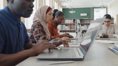 Ders sırasında dizüstü bilgisayar kullanan göçmenler için eğitim merkezinde masada oturan etnik çeşitliliğe sahip bir grup öğrenci.