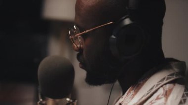 Siyah gözlüklü adamın mikrofona bir şey söylediği yakın plan, kulaklığı açık, yanal görüş.