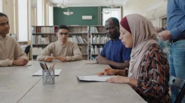 Çok ırklı göçmen öğrencilerden oluşan bir grup masada oturup dil bilgisi sınavı kağıtları alıyor ve bunun üzerinde çalışmaya başlıyorlar.