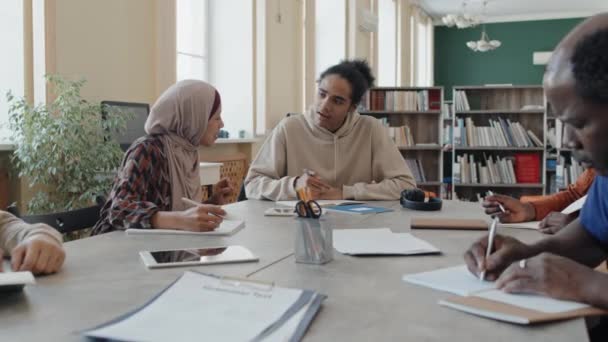 若い黒人男性とイスラム教徒の女性は 移民の学生のためのレッスン中にタスクを書くお互いを助けます — ストック動画