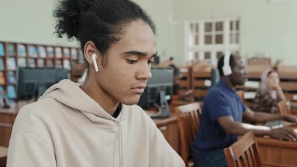 大学図書館でコンピュータを使用した若い黒人移民学生の選択的なフォーカス媒体のクローズアップポートレート — ストック動画
