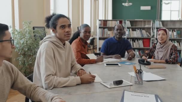 教師の質問に答えるテーブルに座っている移民のための言語クラスに出席する若い黒人男性 — ストック動画