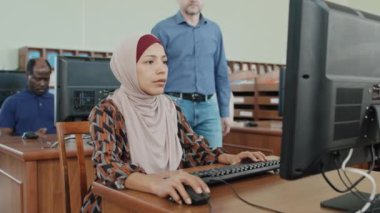 Kütüphanedeki masaüstü bilgisayarında görev yapan, tesettürlü Müslüman bir kadının seçmeli odak fotoğrafı.