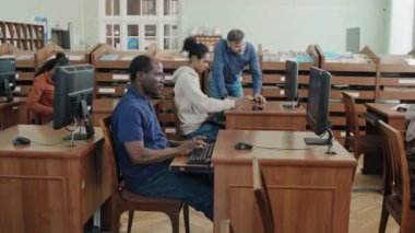 Okul kütüphanesindeki bilgisayarlarda online test yapan bir grup siyah göçmen öğrenci, yetişkin beyaz bir öğretmenin görevi anlamalarına yardımcı olması