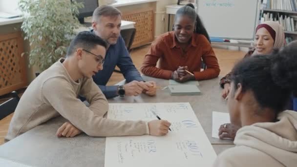Этнически Разнообразные Иммигранты Учитель Сидят Столом Классе Работая Над Плакатом — стоковое видео