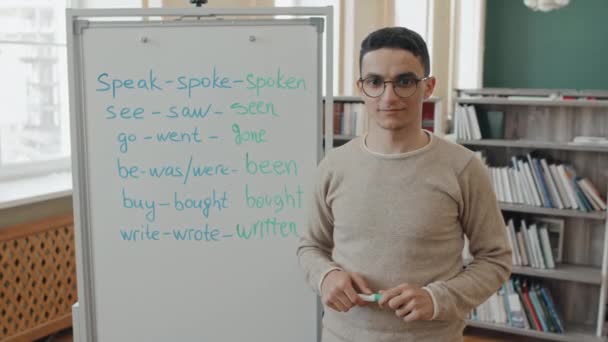 中肖像画 年轻的中东男子戴着眼镜 站在白板前看着摄像机 参加英语课 — 图库视频影像