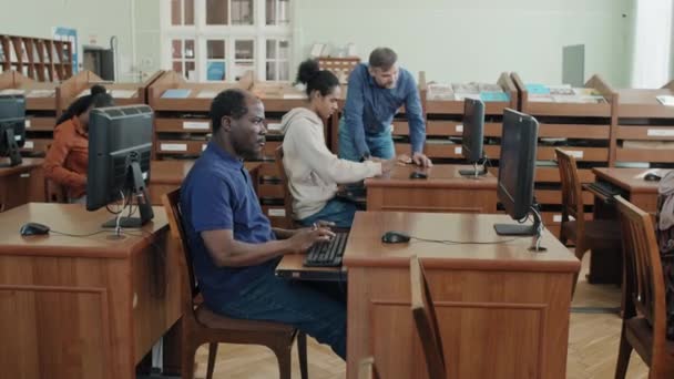 一群在学校图书馆的桌上型计算机上做在线测试的黑人移民学生 他们是一位成熟的高加索教师 帮助其中一个人理解了这个任务 — 图库视频影像
