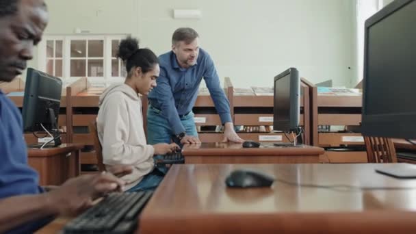 成熟白人教师帮助年轻黑人学生完成计算机任务的选择性聚焦拍摄 — 图库视频影像