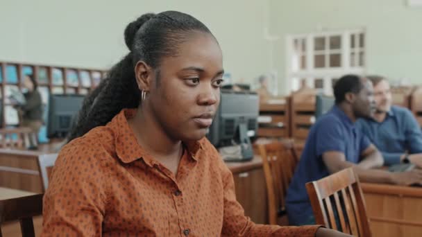 高校图书馆工作的年轻黑人女生带耳机工作计算机的中等特写选择性镜头 — 图库视频影像
