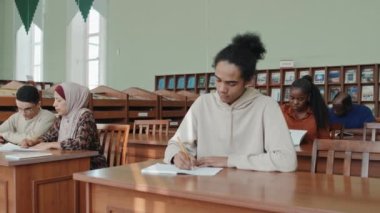 Genç siyahi adam ve çok ırklı sınıf arkadaşları ders sırasında masalarında oturup notlar alıyorlar.