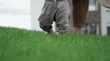 Orta ölçekli, tanınmayan anne ve bebeğin çimenlerde çıplak ayakla yürüdüğü bir sahne.