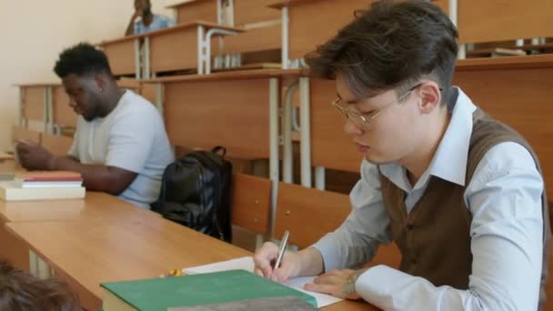 講演中にノートを作る現代アジアの若い大学生の選択的な焦点ショット — ストック動画