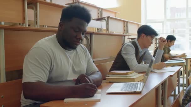 在大学的课堂上 一群不同种族的学生坐在课桌前做笔记 — 图库视频影像